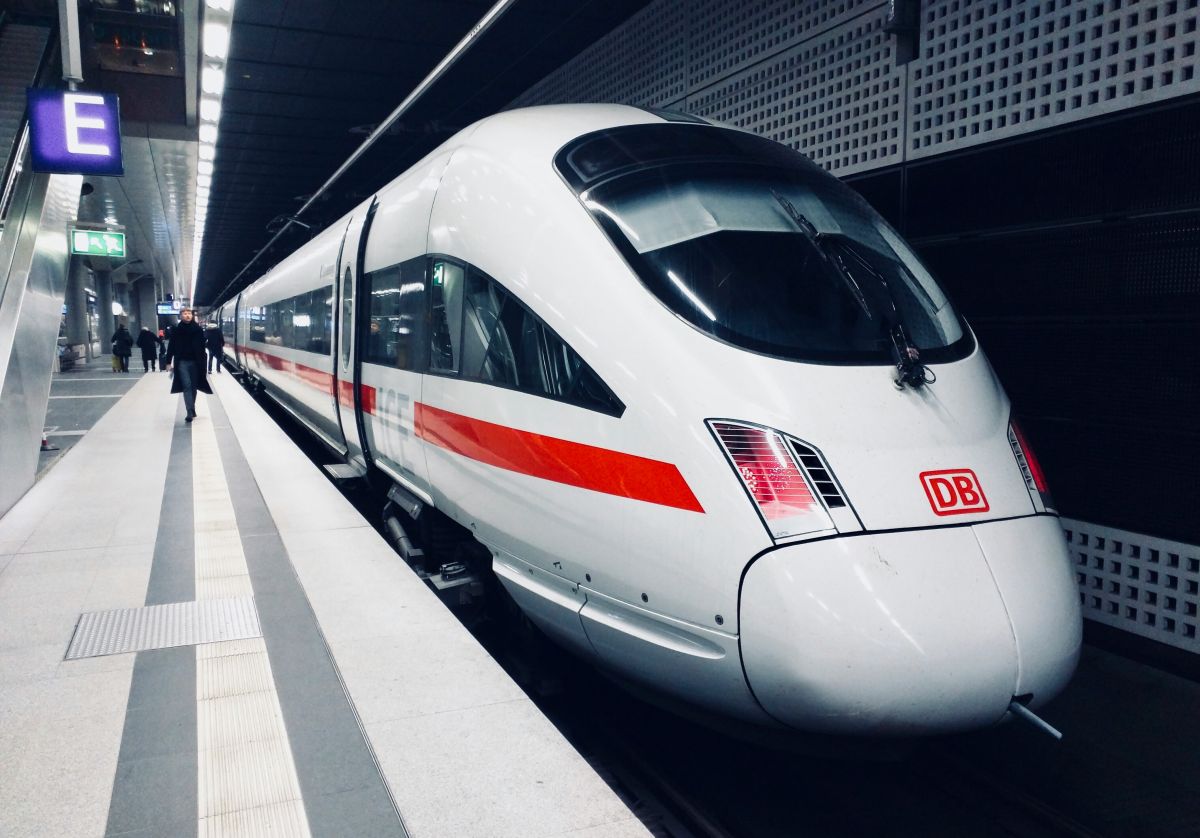 Weißer ICE-Zug mit rotem Streifen steht im beleuchteten Bahnhof an Gleis E, eine Person geht am Bahnsteig entlang.